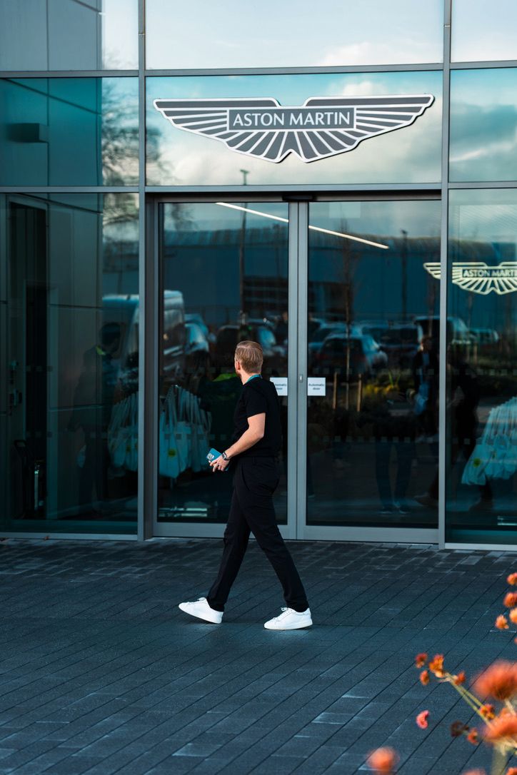 Modern Aston Martin dealership exterior with glass facade and iconic winged logo displayed above the entrance.