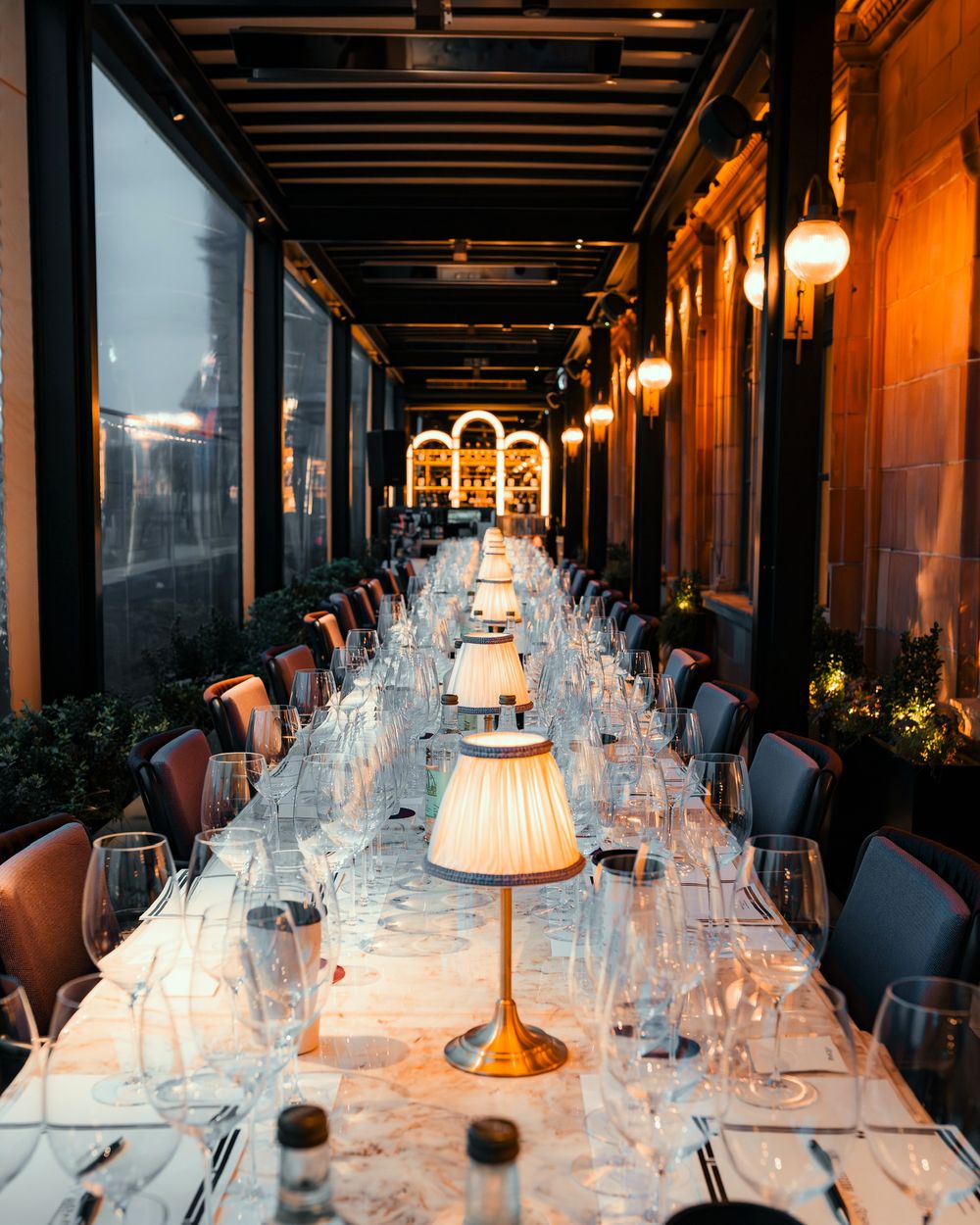 Elegant long dining table setup with glowing table lamps and wine glasses in an upscale restaurant interior.