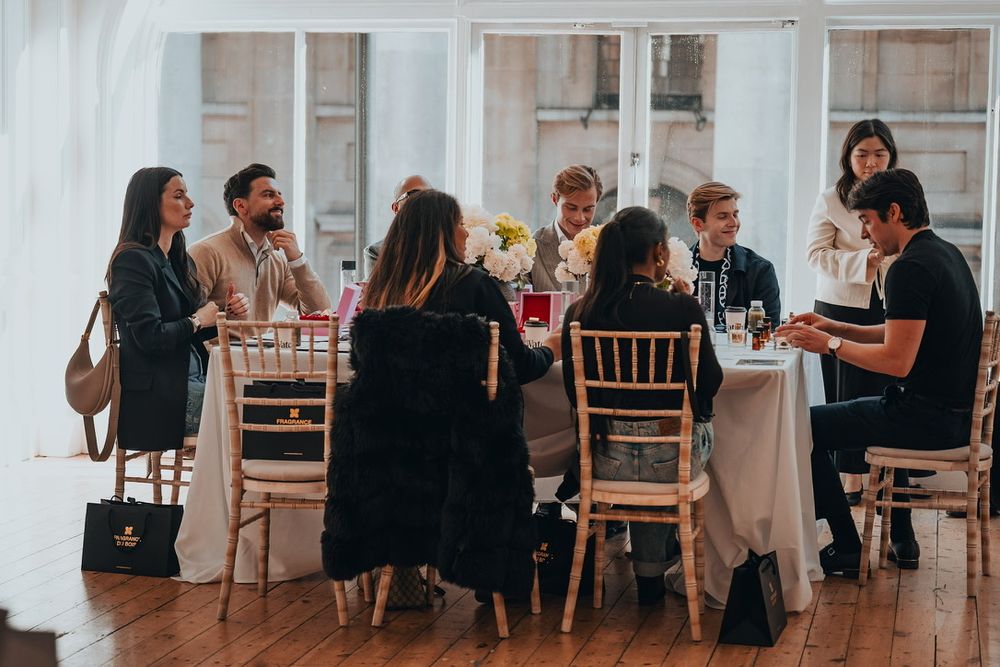 People seated at long tables during an indoor event with white draping and natural lighting.
