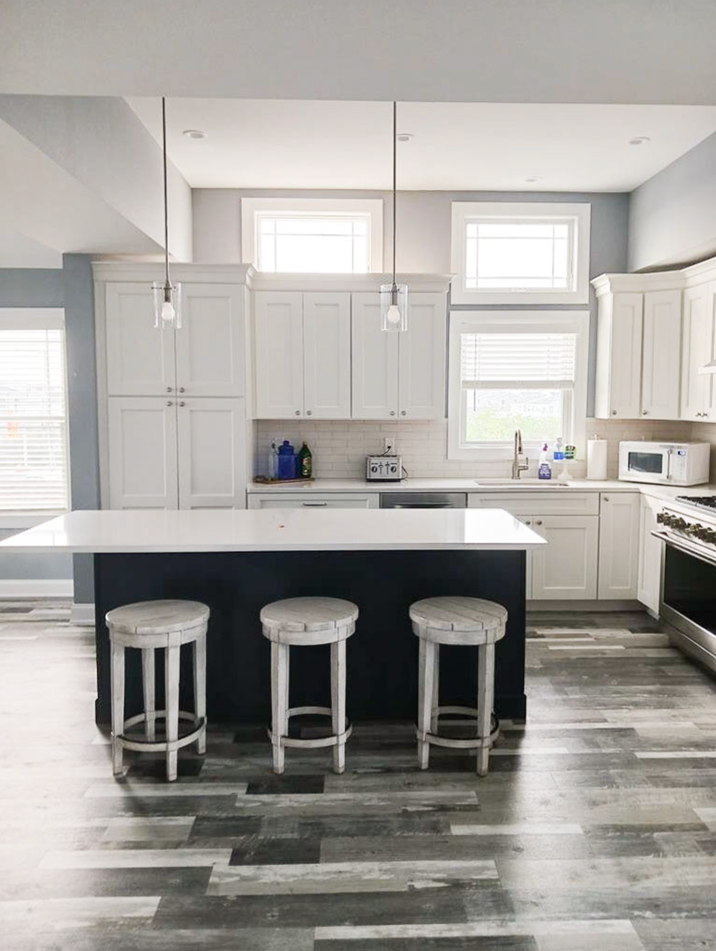 Contemporary white kitchen with dark island, bar stools and gray flooring.