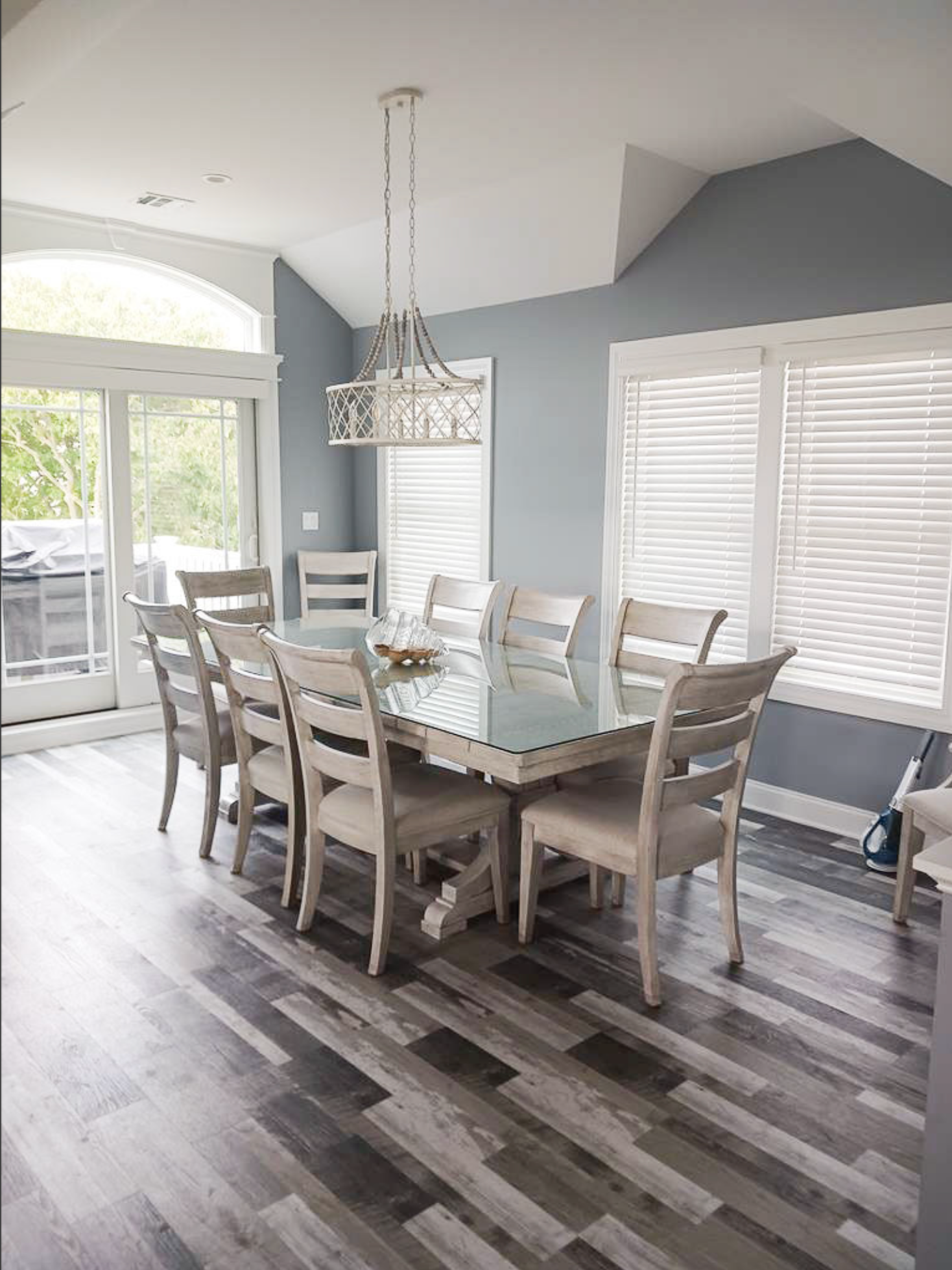 Modern dining room with gray walls, rustic flooring and ladder-back chairs around large table.