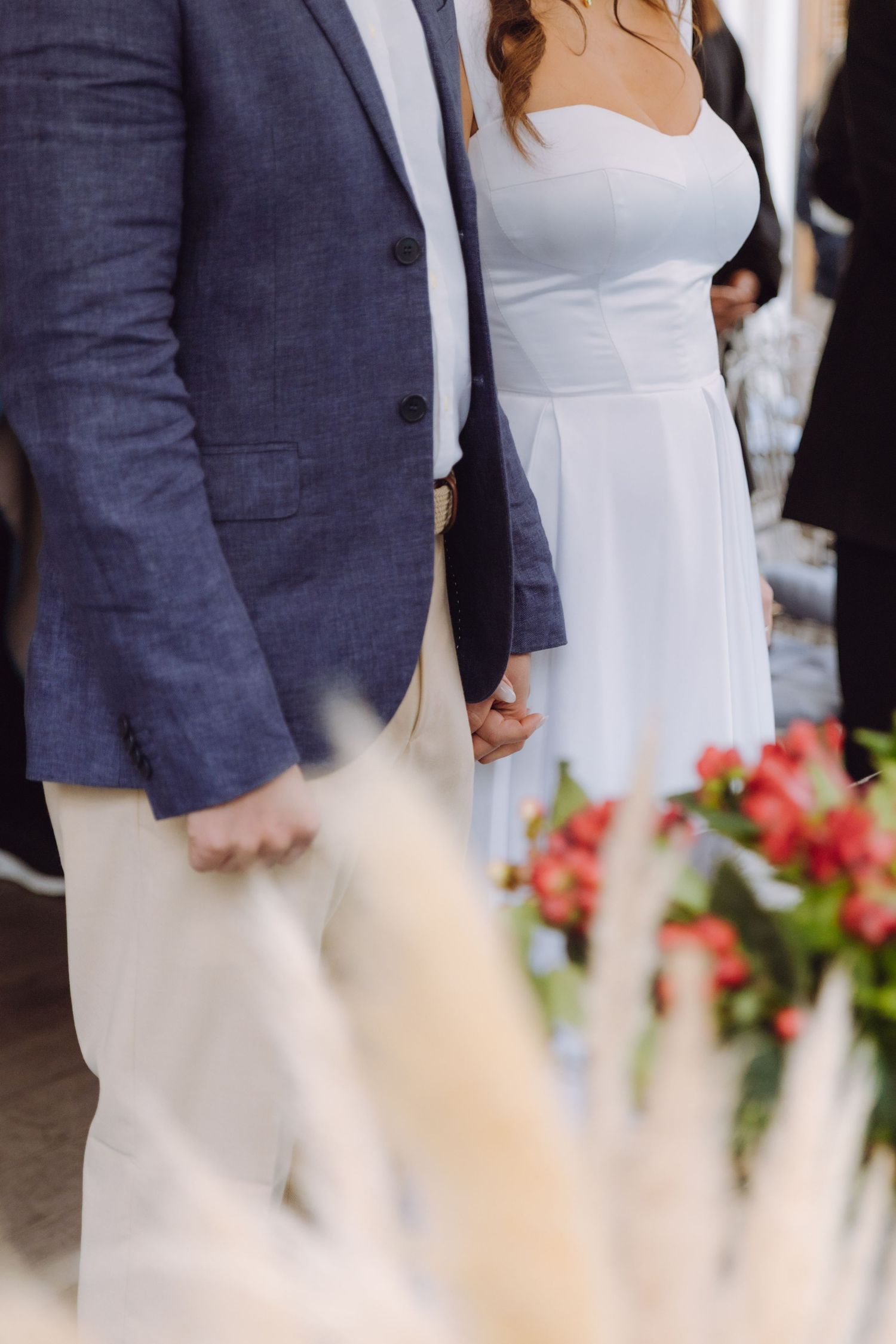 Bride in white dress and groom in blue blazer hold hands during outdoor wedding ceremony.