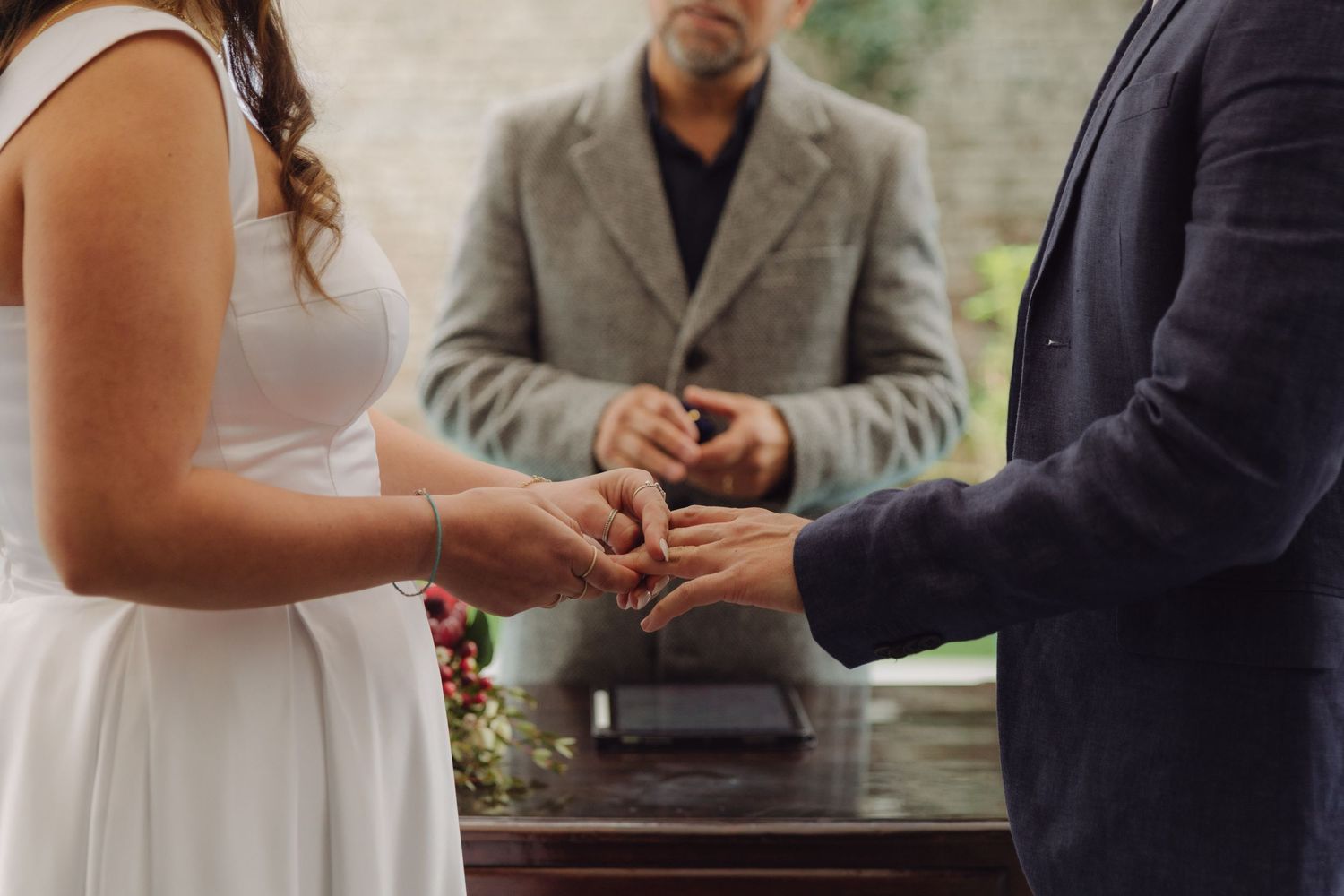 Close-up of couple exchanging wedding rings with officiant presiding at outdoor ceremony.