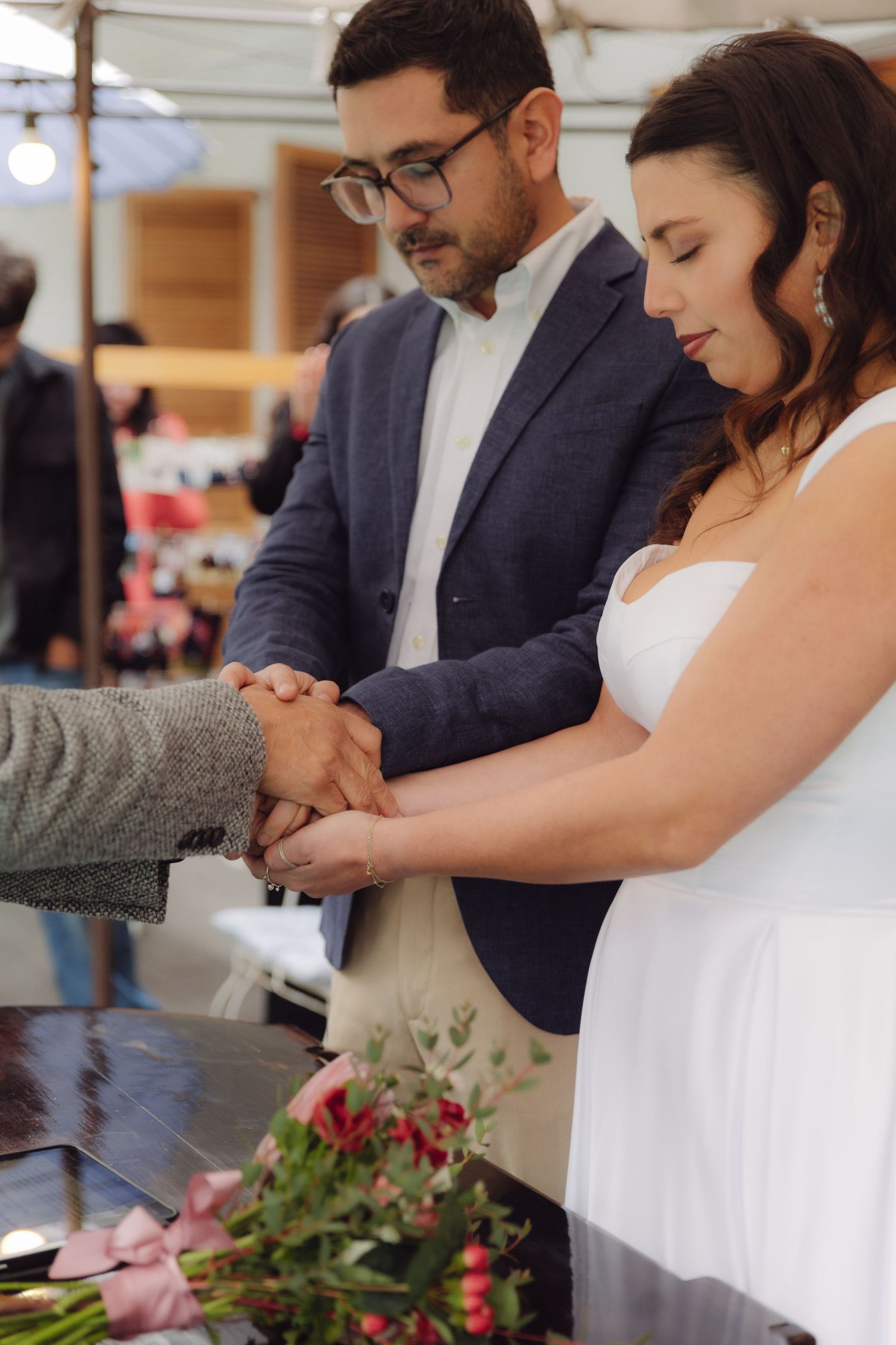 Officiant joins hands of bride and groom over ceremony table during wedding ritual.