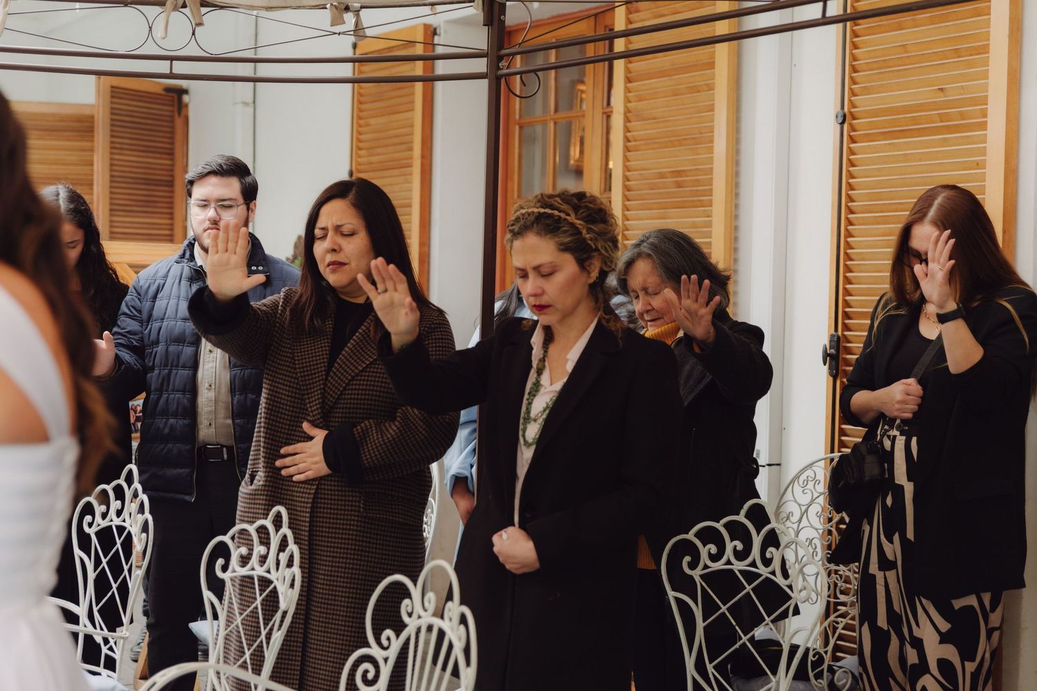 Wedding guests raising their hands in blessing during an outdoor ceremony.