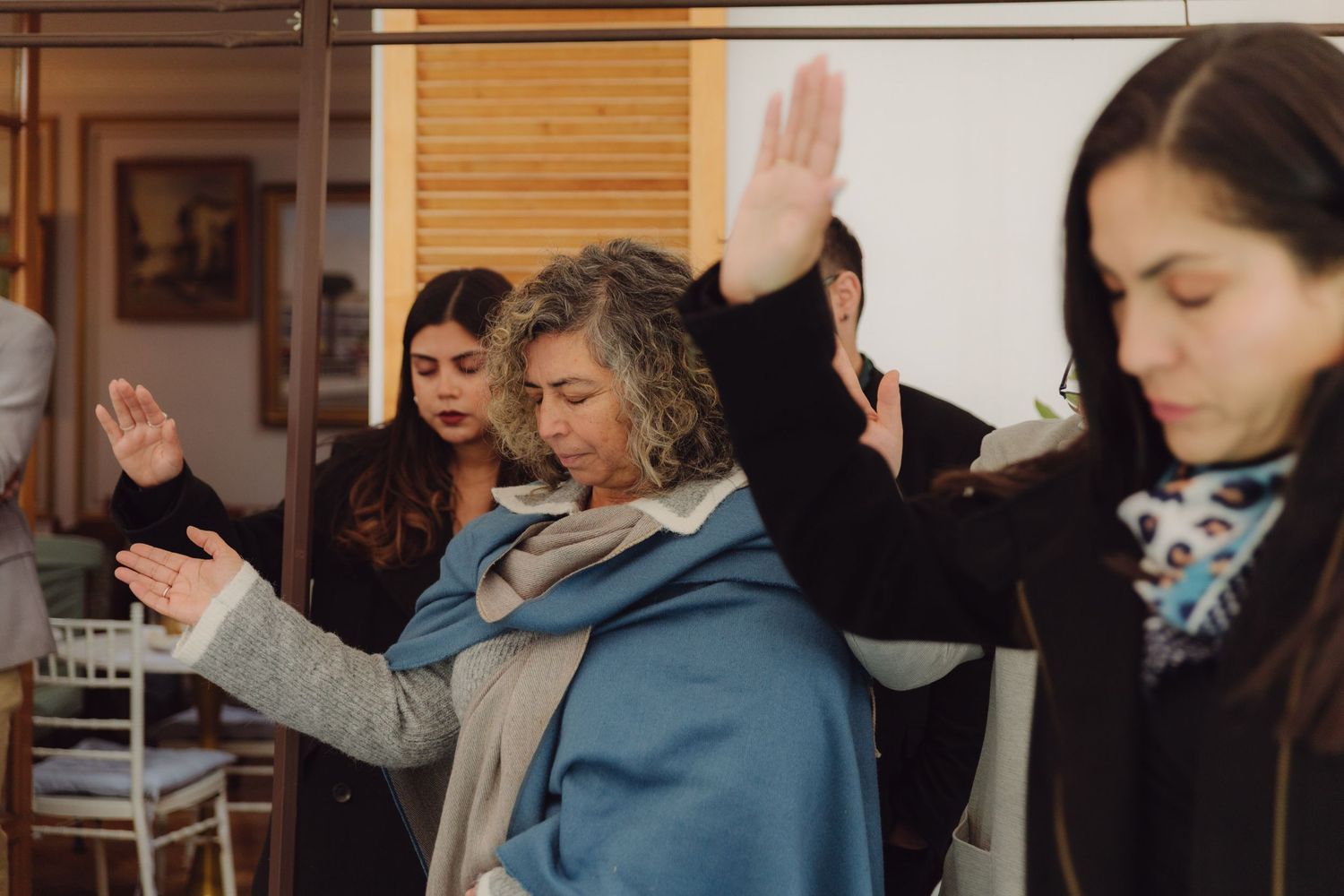 Wedding guests raising hands in prayer during an indoor ceremony blessing.