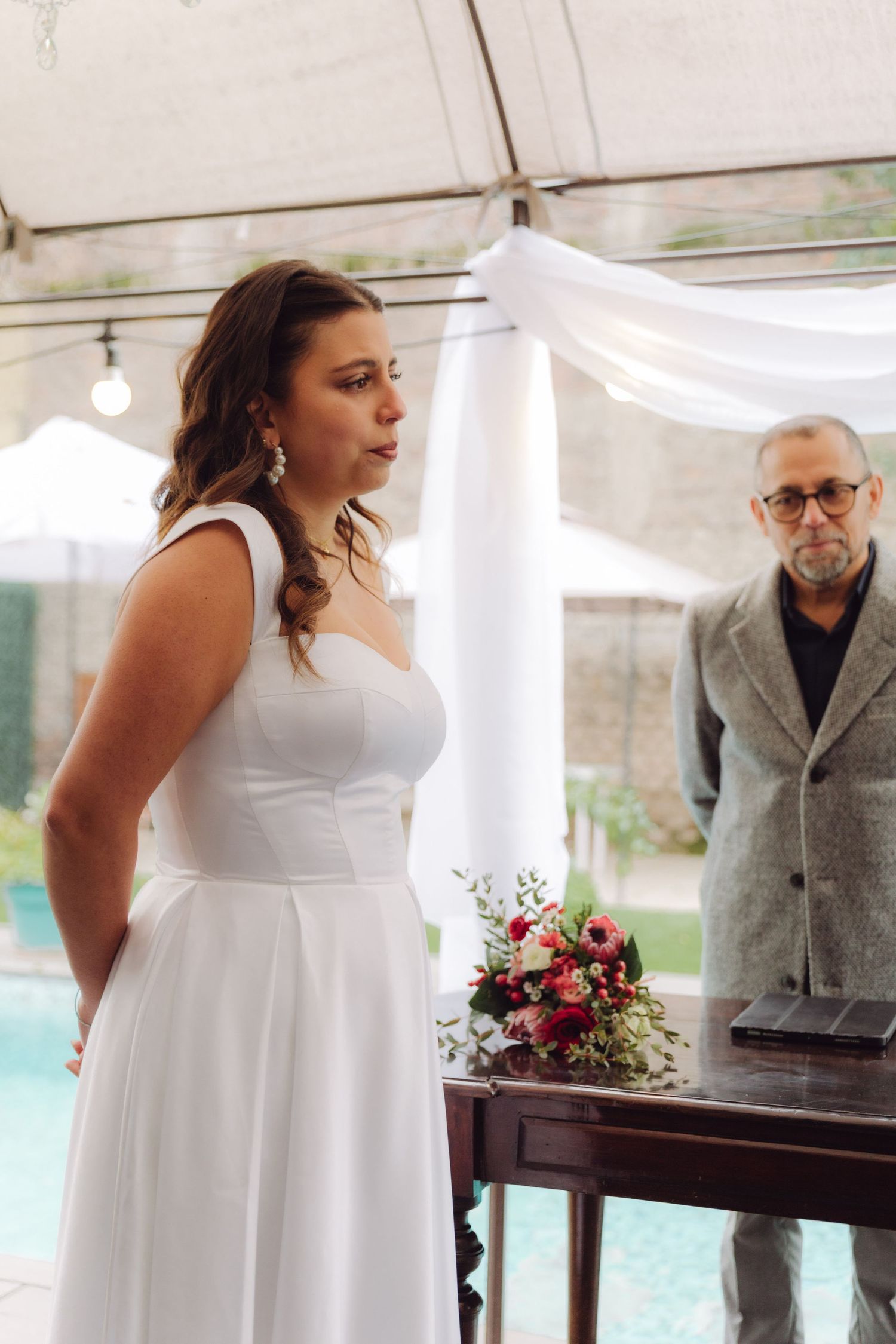 Beautiful bride in white gown reciting vows at outdoor wedding ceremony.