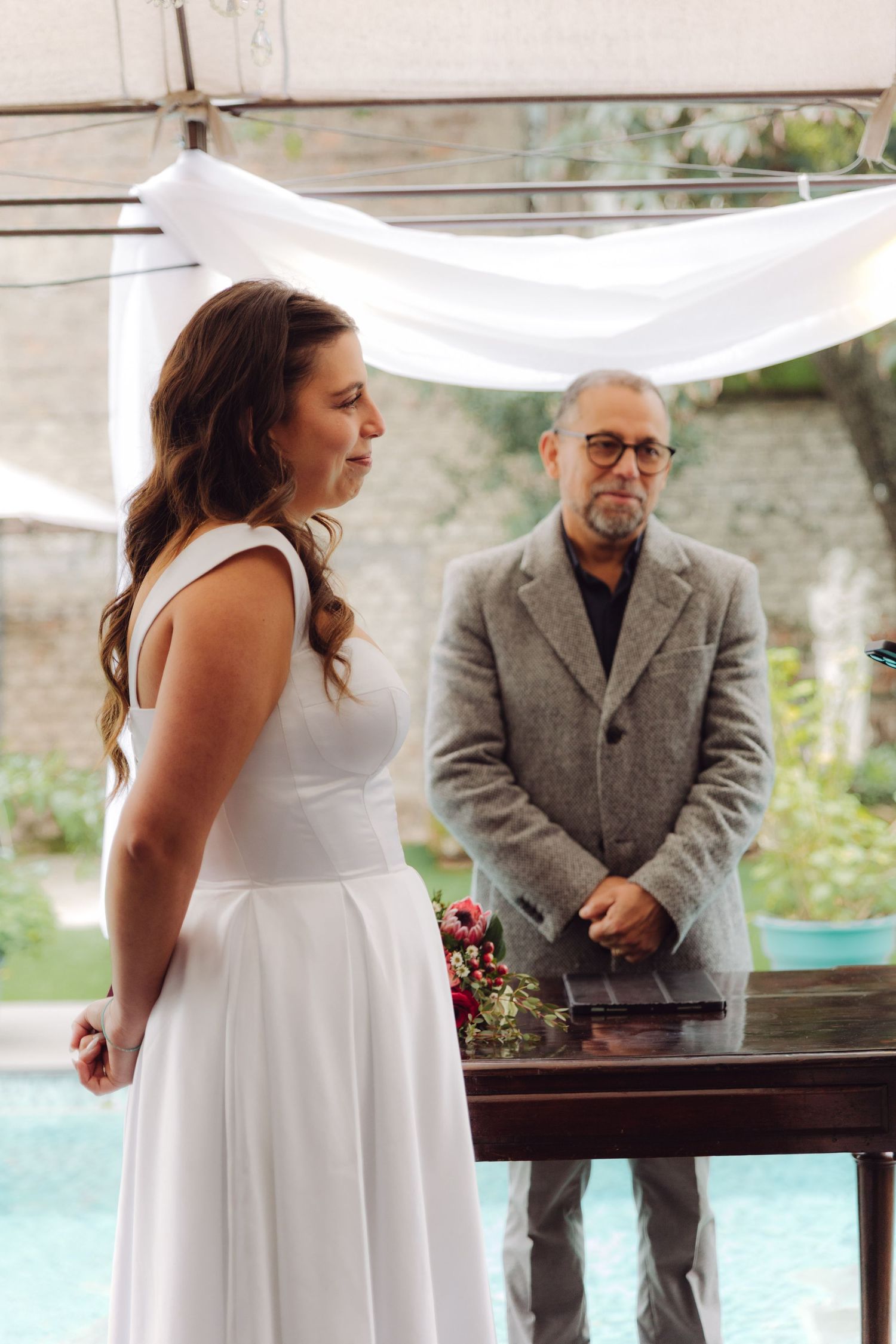 Elegant bride in white gown speaking vows at outdoor poolside wedding.