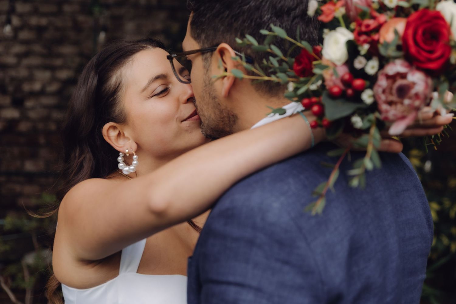 Bride and groom share a romantic kiss during outdoor wedding ceremony with floral bouquet.