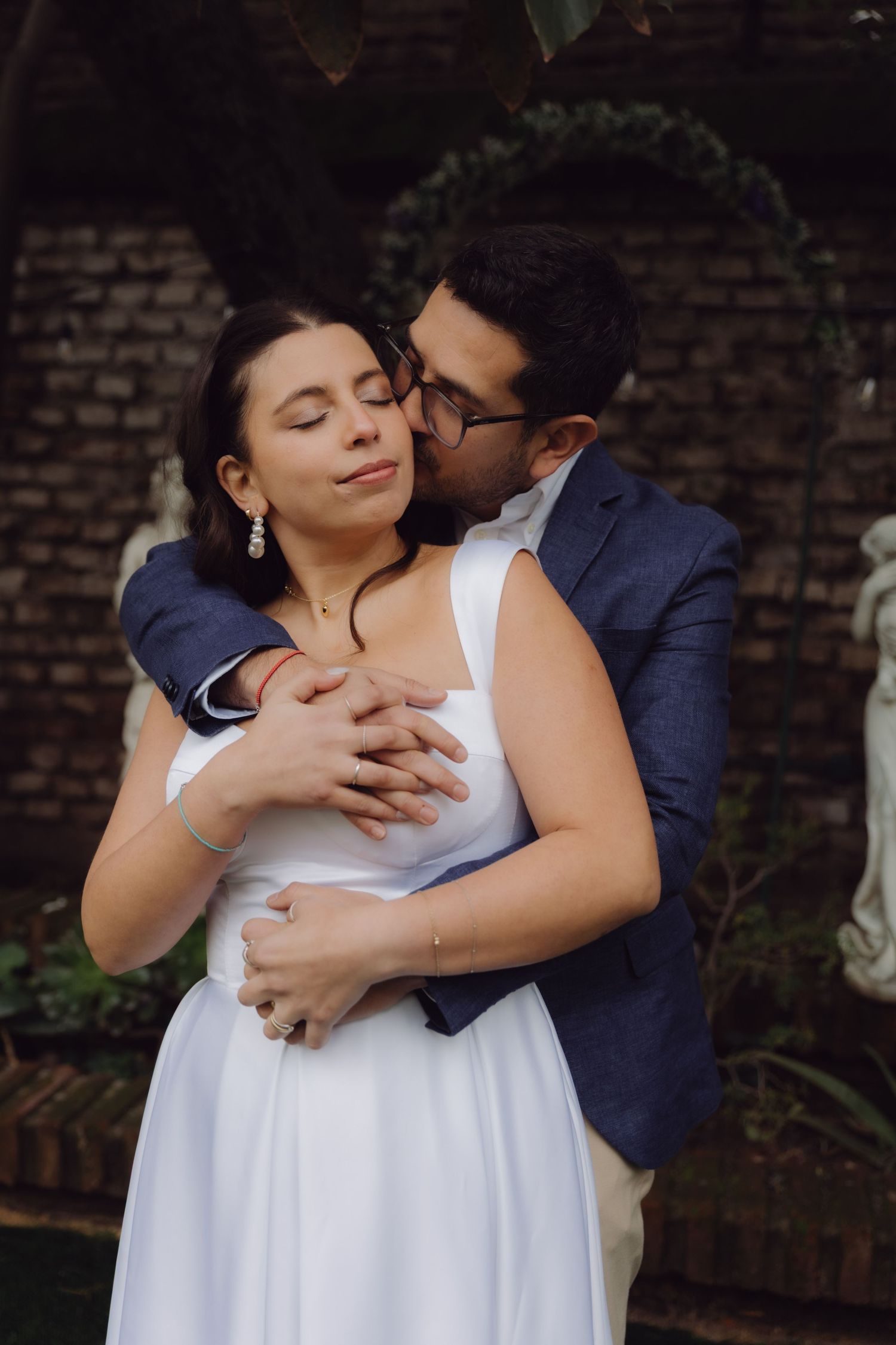 Groom kisses bride on cheek as she closes her eyes in a loving embrace outdoors.
