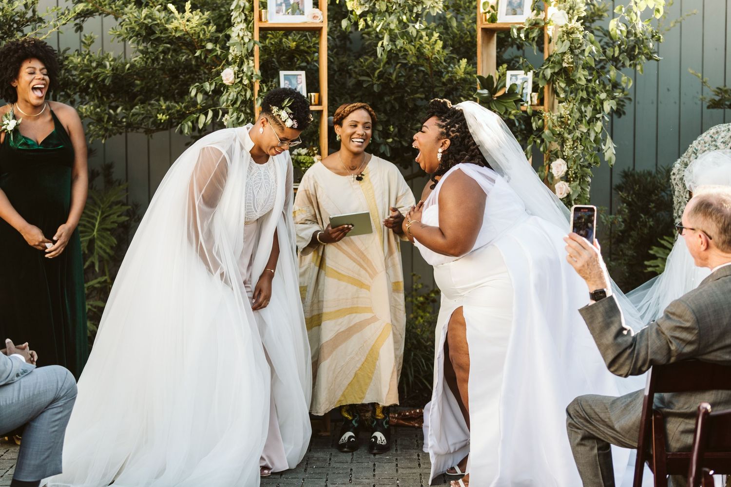 Wedding party stands under a large tree with twisting branches during an outdoor celebration.