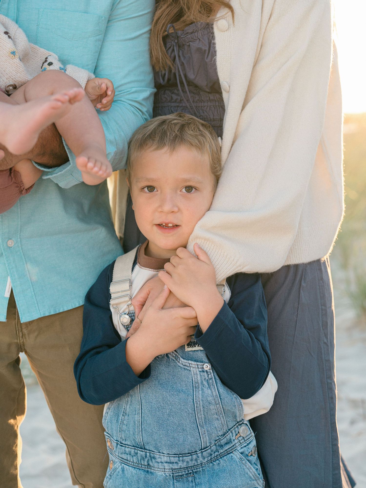 A close up image of toddle boy's face with his arms wrapped around his mother's arm.