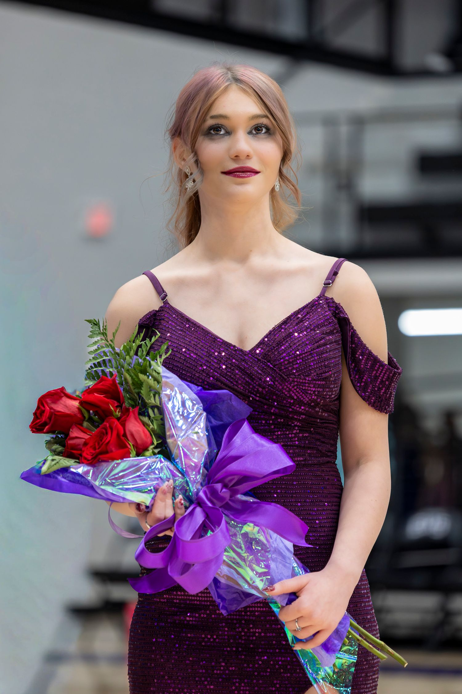 A person in a sparkly purple evening gown holds a vibrant bouquet with red roses and purple ribbons.