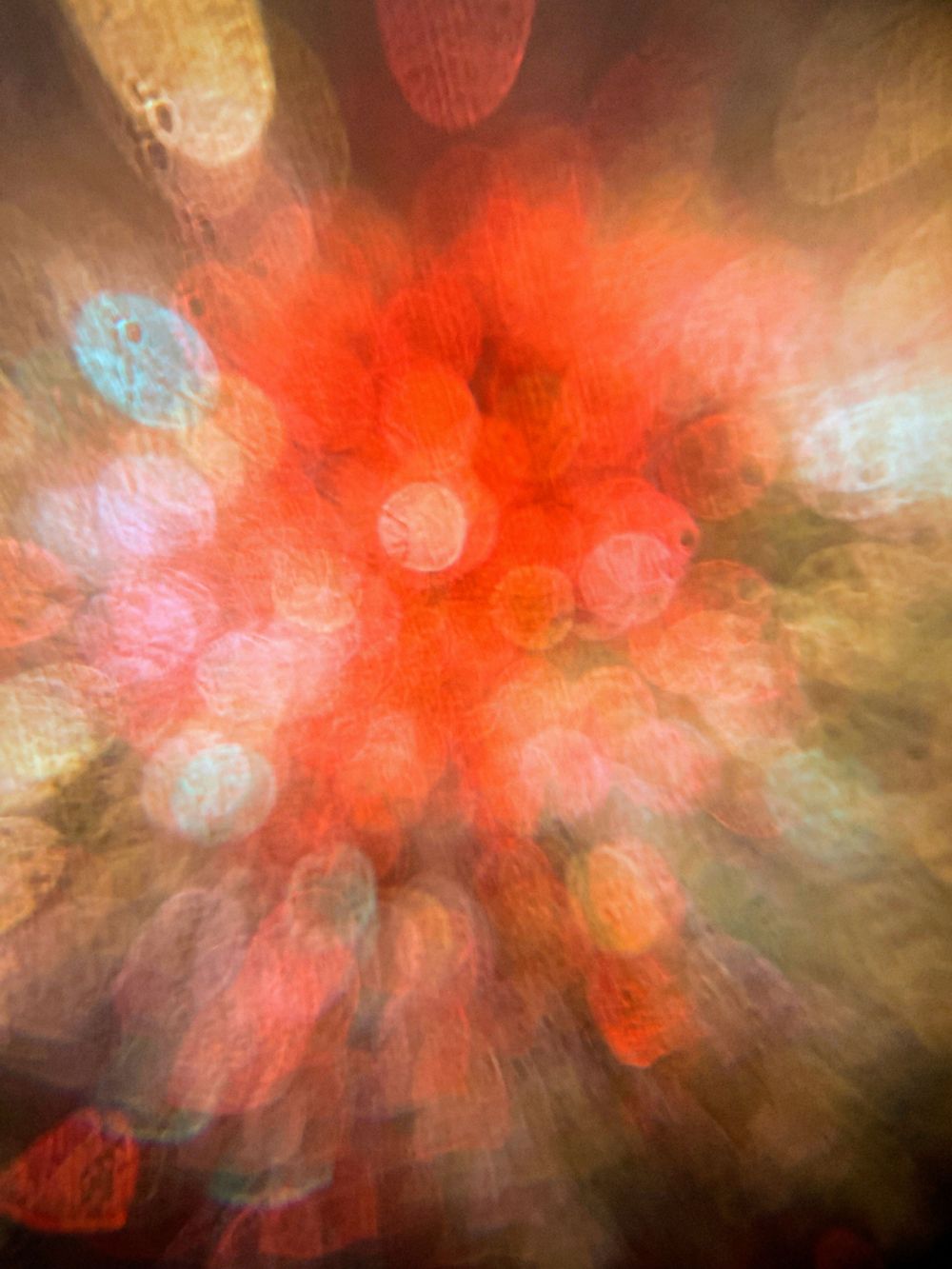 Abstract blurred image with bright red and orange burst in center surrounded by soft bokeh lights and dark edges.