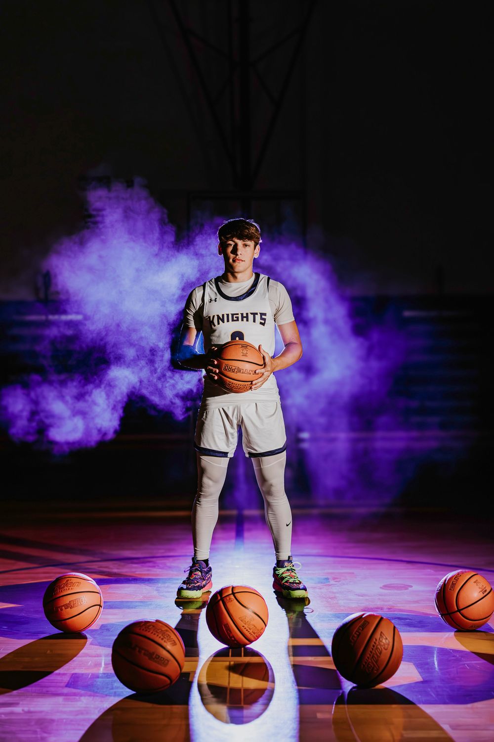 Basketball player in Knights uniform surrounded by basketballs and purple smoke.