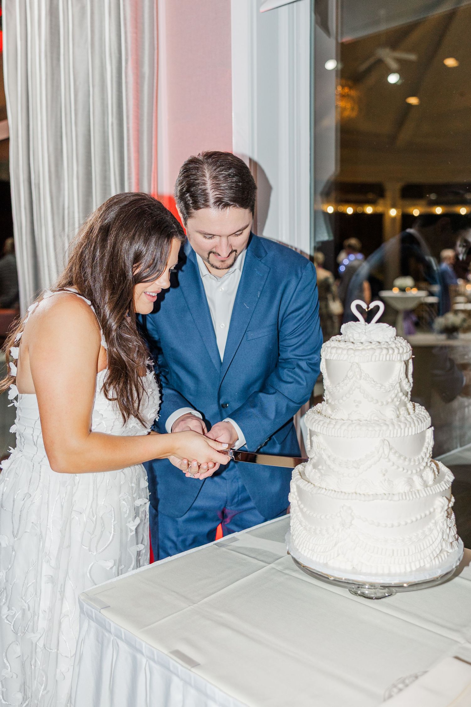 A couple cuts into their elegant white wedding cake topped with a swan decoration at their reception.