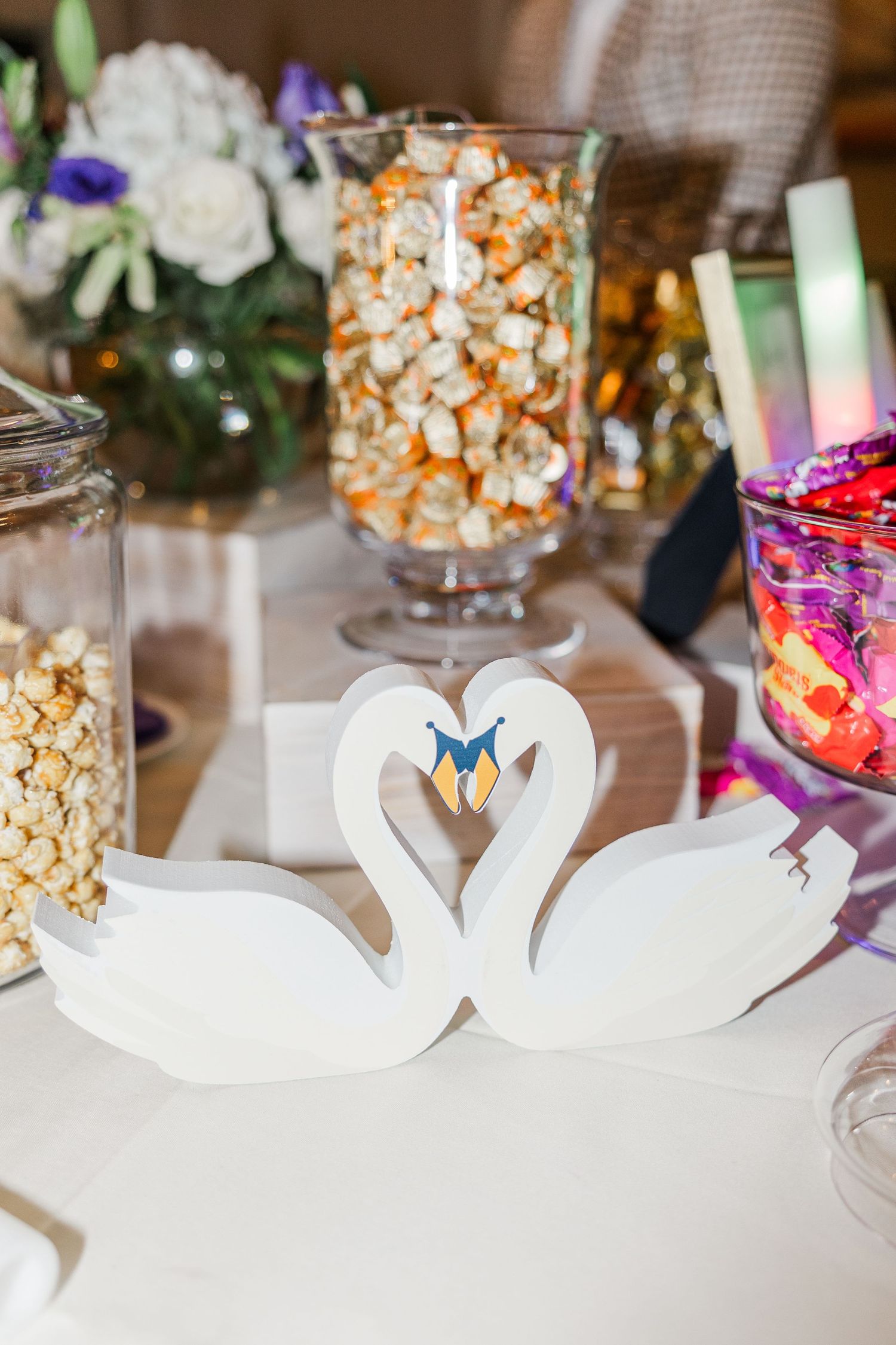 White decorative swan centerpieces displayed on tables with glass jars filled with popcorn at an elegant event.
