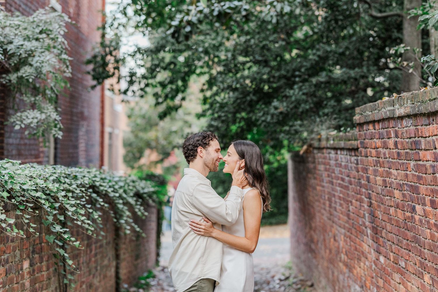 A couple shares a romantic moment walking along a rustic brick wall path surrounded by lush greenery.