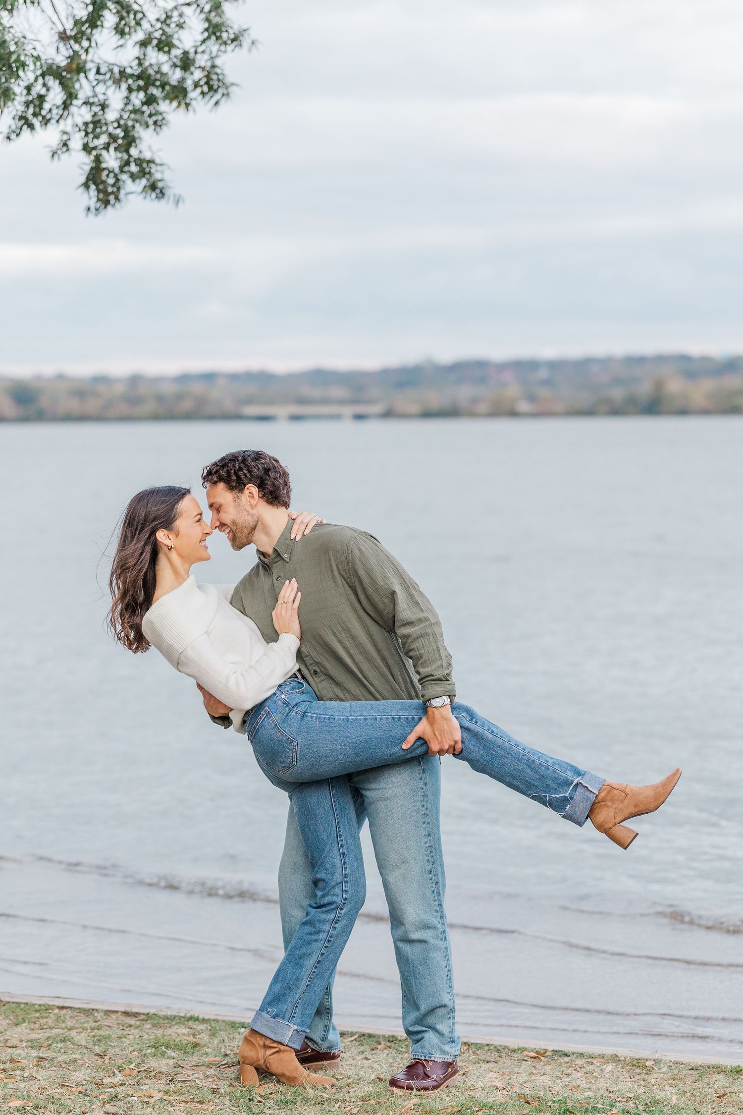 A romantic couple shares a playful dip kiss pose by the waterfront on a cloudy day.