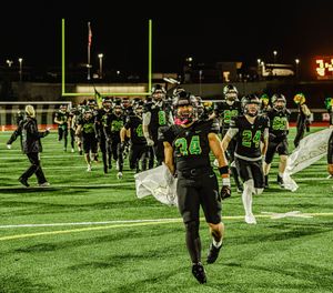 Football team in green and black uniforms walking off field under stadium lights at night.