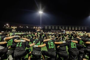 Stadium crowd watches intently from the stands during a nighttime football game under bright lights.