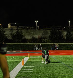 Football player in green jersey kneels on illuminated red turf field during nighttime game.