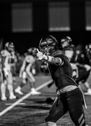 Football player in black uniform prepares to throw the ball during a nighttime game on the field.