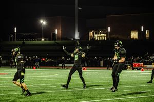 Football players compete under bright stadium lights during a nighttime game on an artificial turf field.