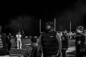 Silhouettes of football players and spectators stand against a dark night sky during a game.