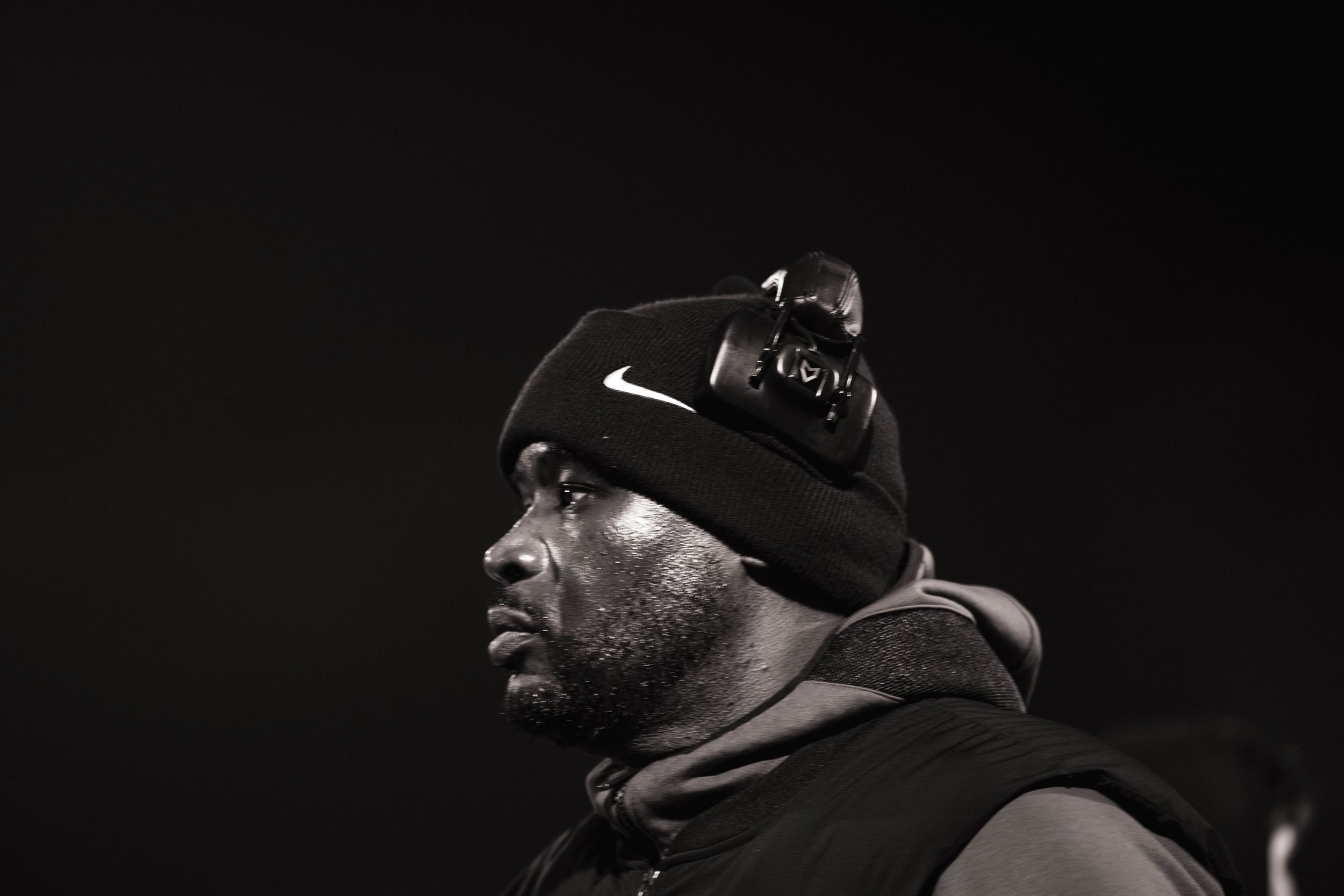 A dramatic black and white profile shot of someone wearing a Nike beanie and hoodie against a dark background.