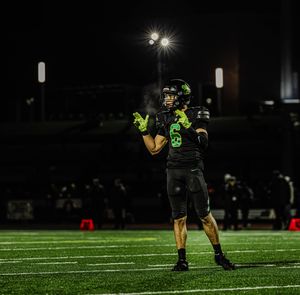 Football players line up on an illuminated field at night during a game under bright stadium lights.