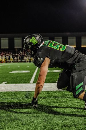 Football players in black and green uniforms perform push-ups on the turf field during a game.