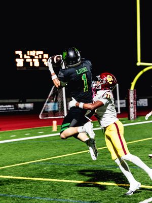 Two football players compete for the ball near the goal post during a night game on artificial turf.