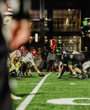 Football players in a tight formation prepare for a snap on a brightly lit field during a night game.