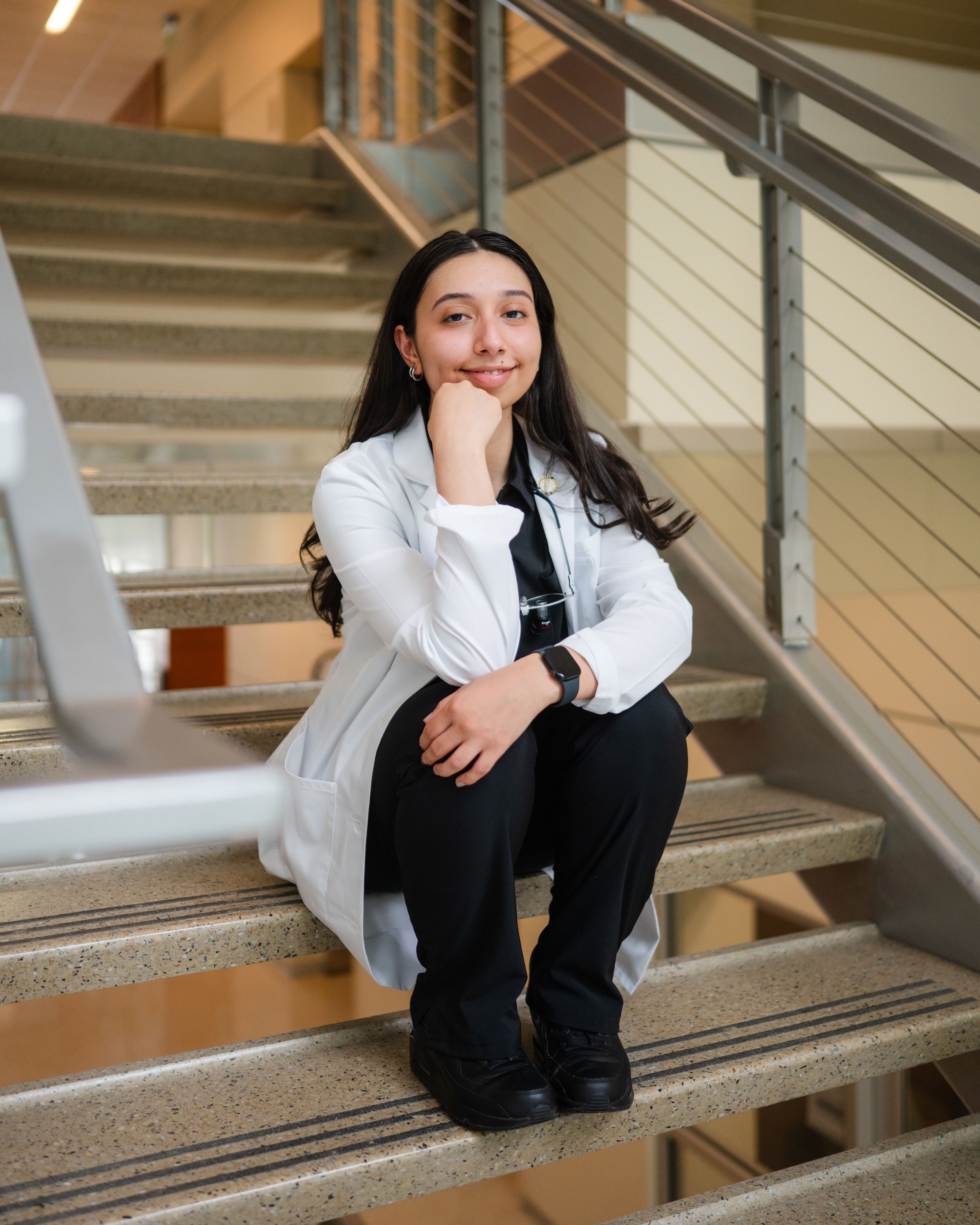 A person in a white blazer and dark pants sits casually on modern architectural stairs.