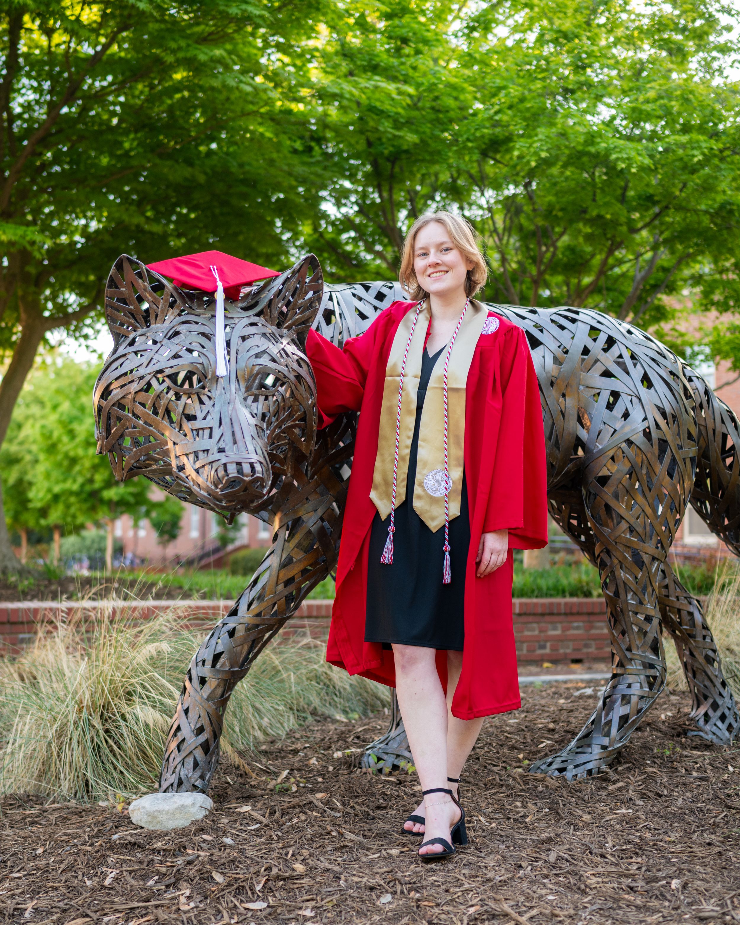 A metal wire art sculpture of a leopard stands in a garden setting with lush green trees and landscaping in the background.