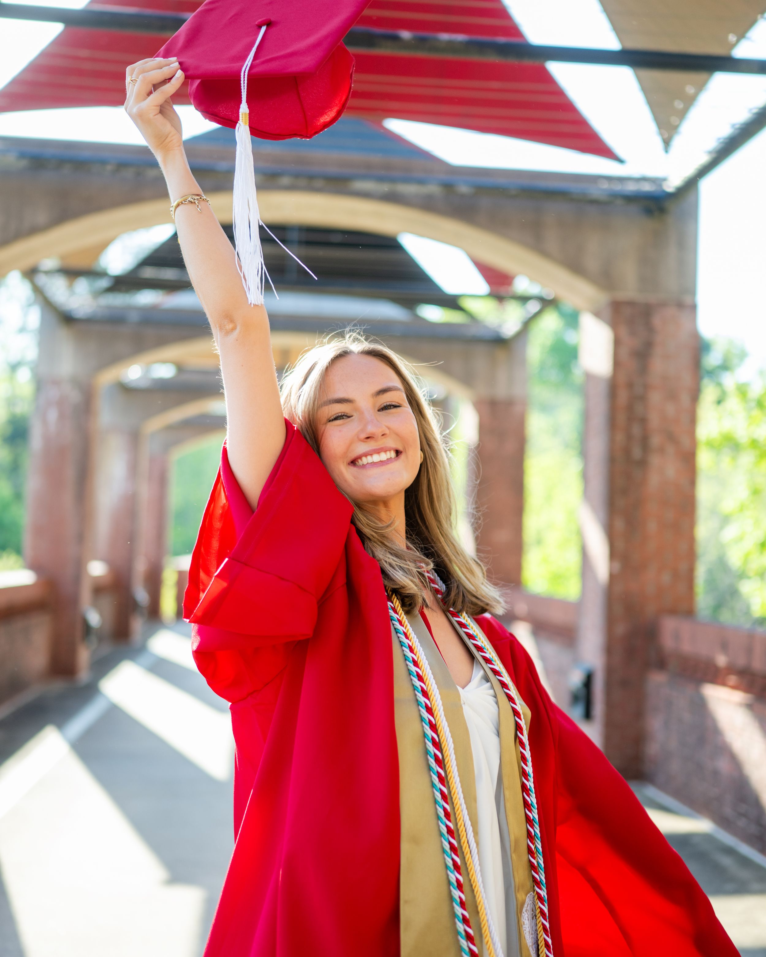 Graduate in red cap and gown celebrates joyfully during outdoor graduation ceremony with columns in background.