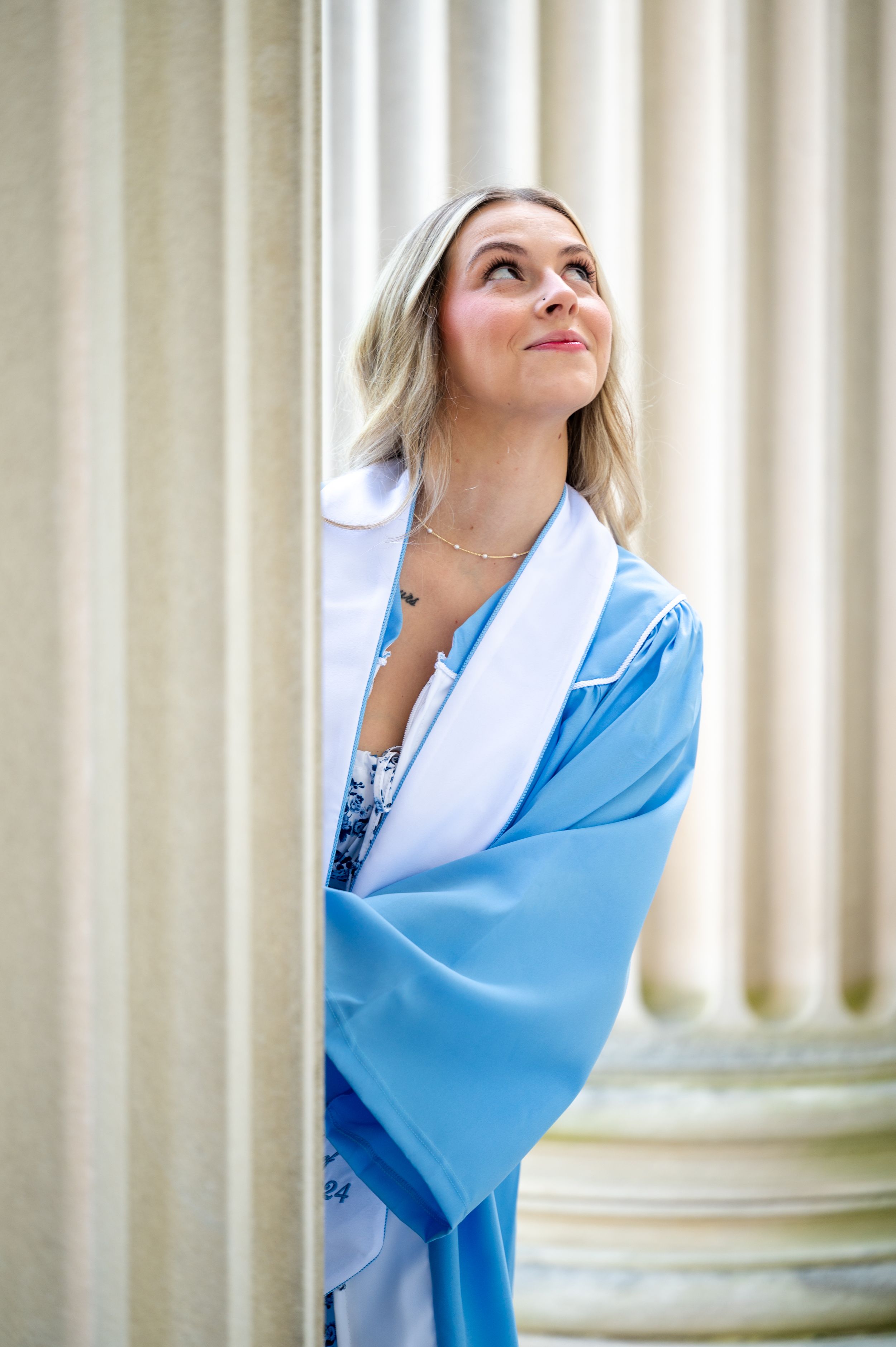 A person wearing a light blue wrap gazes upward while standing near white architectural columns.