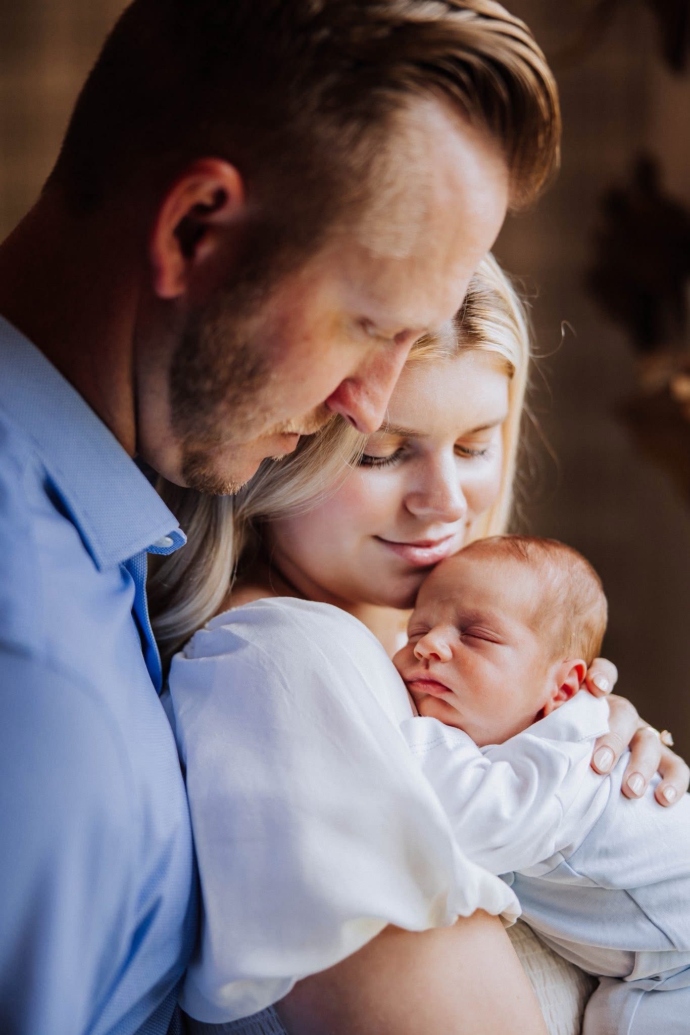New parents lovingly gazing at their sleeping newborn baby wrapped in a white blanket.