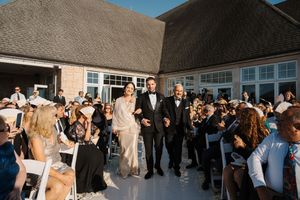 Wedding party and guests gather outside a white building during sunset for group photos.