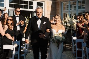 Wedding ceremony recessional at an elegant venue with guests watching from wooden chairs as couple walks down aisle.