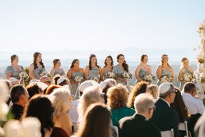 A large group of wedding guests seated outdoors at a ceremony with an ocean view in the background.