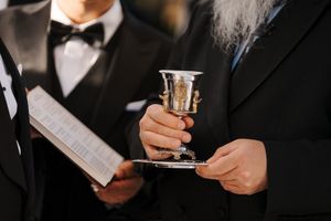 A silver Kiddush cup and prayer book being held during a Jewish ceremony or service.