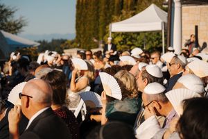 A large crowd of spectators wearing white hats and caps gathered outdoors at a daytime event.