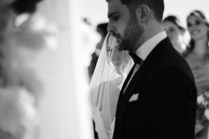A black and white wedding ceremony photo shows a couple exchanging vows at the altar with guests looking on.