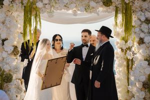 Elegant wedding ceremony with floral arch and white decor as couple exchanges vows.