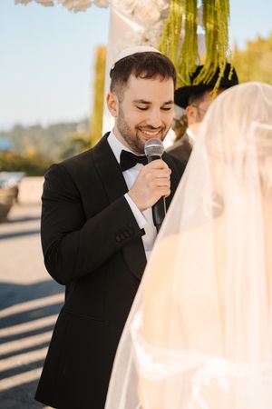 Emotional groom wipes tears from his eyes during outdoor wedding ceremony at sunset.