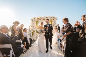 Wedding guests celebrate and dance during an outdoor reception under string lights at sunset.