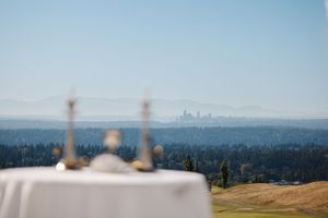 A table set for dining overlooks a scenic cityscape view with distant skyscrapers visible through forested hills.