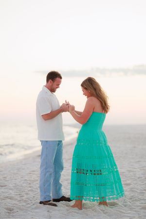 A couple shares a romantic moment on a white sandy beach at sunset wearing turquoise and white outfits.